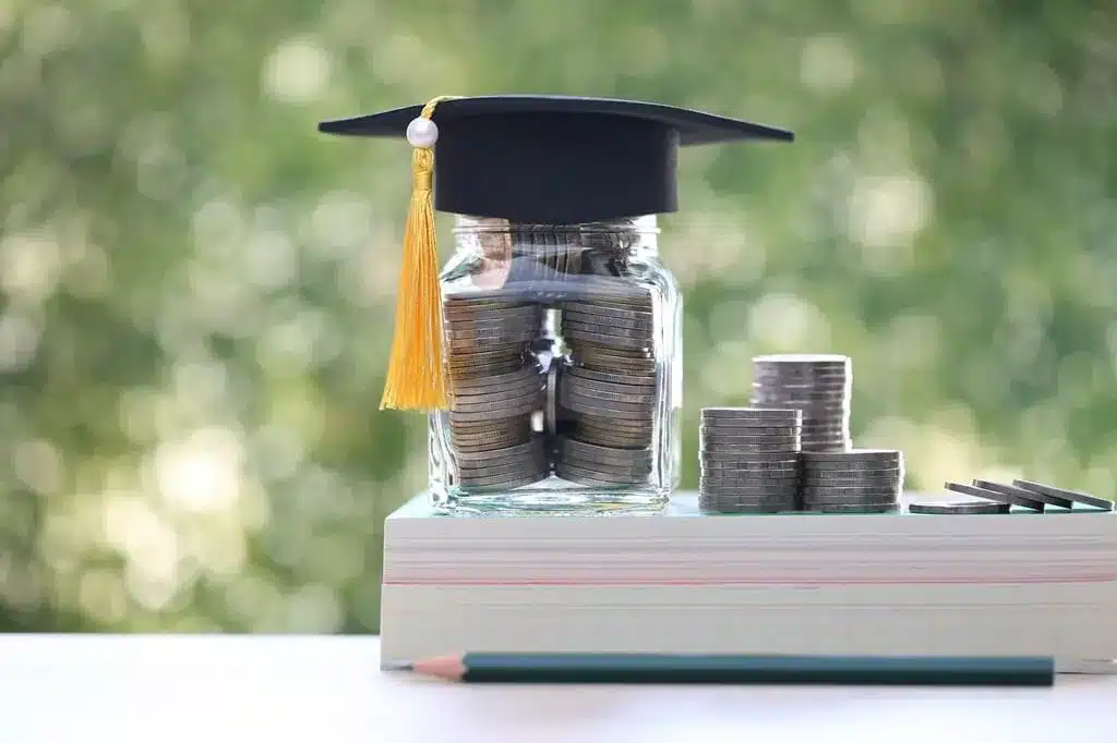 vidro cheio de moedas em cima de livro e com capelo em cima